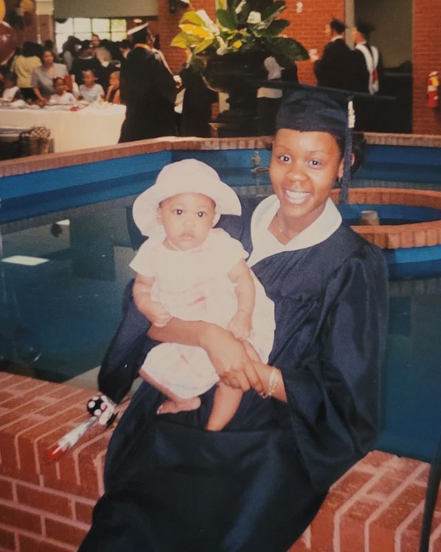 Andrene Ward-Hammond in black graduation dress carrying her daughter in her arms.